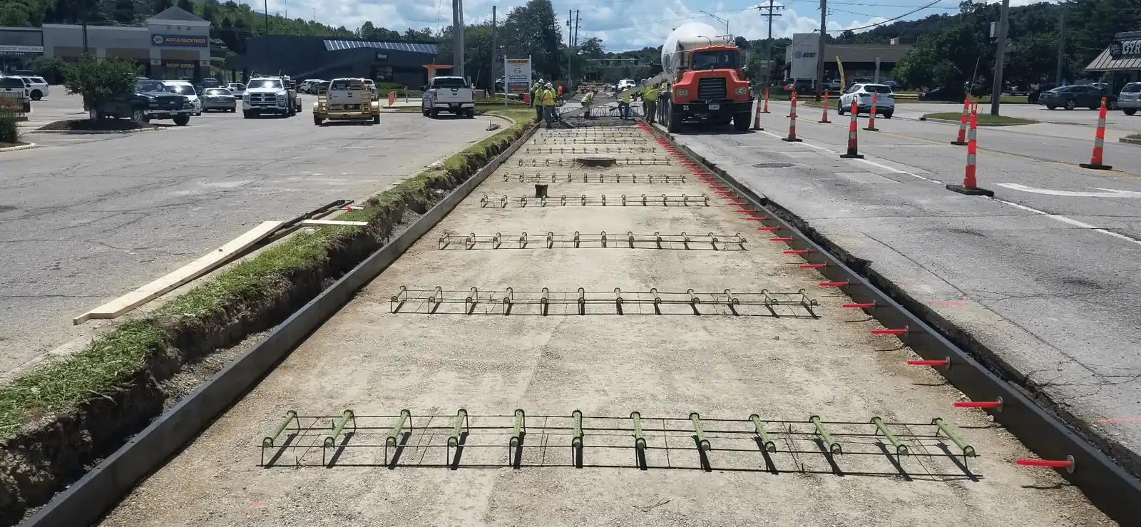 A Raineri crew pouring a concrete pavement section over dowel baskets, with a mixer truck and cones